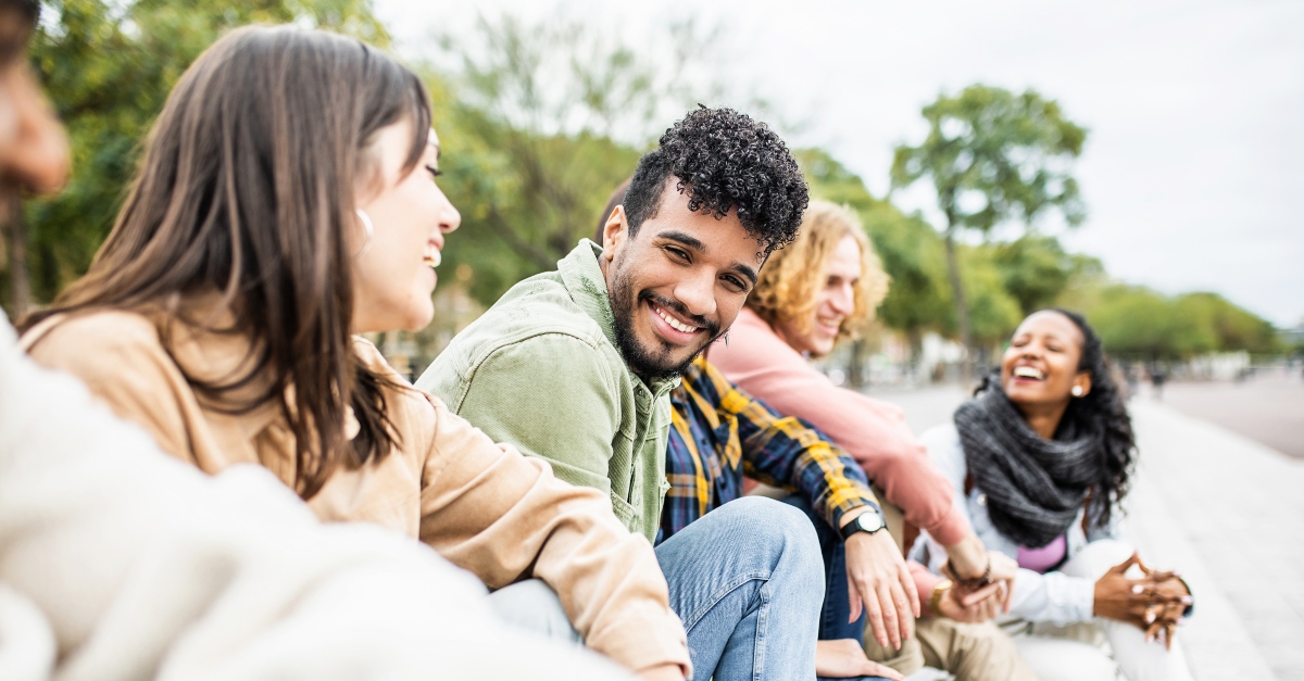Diverse group of young people laughing together - Hispanic latin man smiling at camera while having fun with multiracial friends in city street - Friendship, unity and millennial colleagues concept